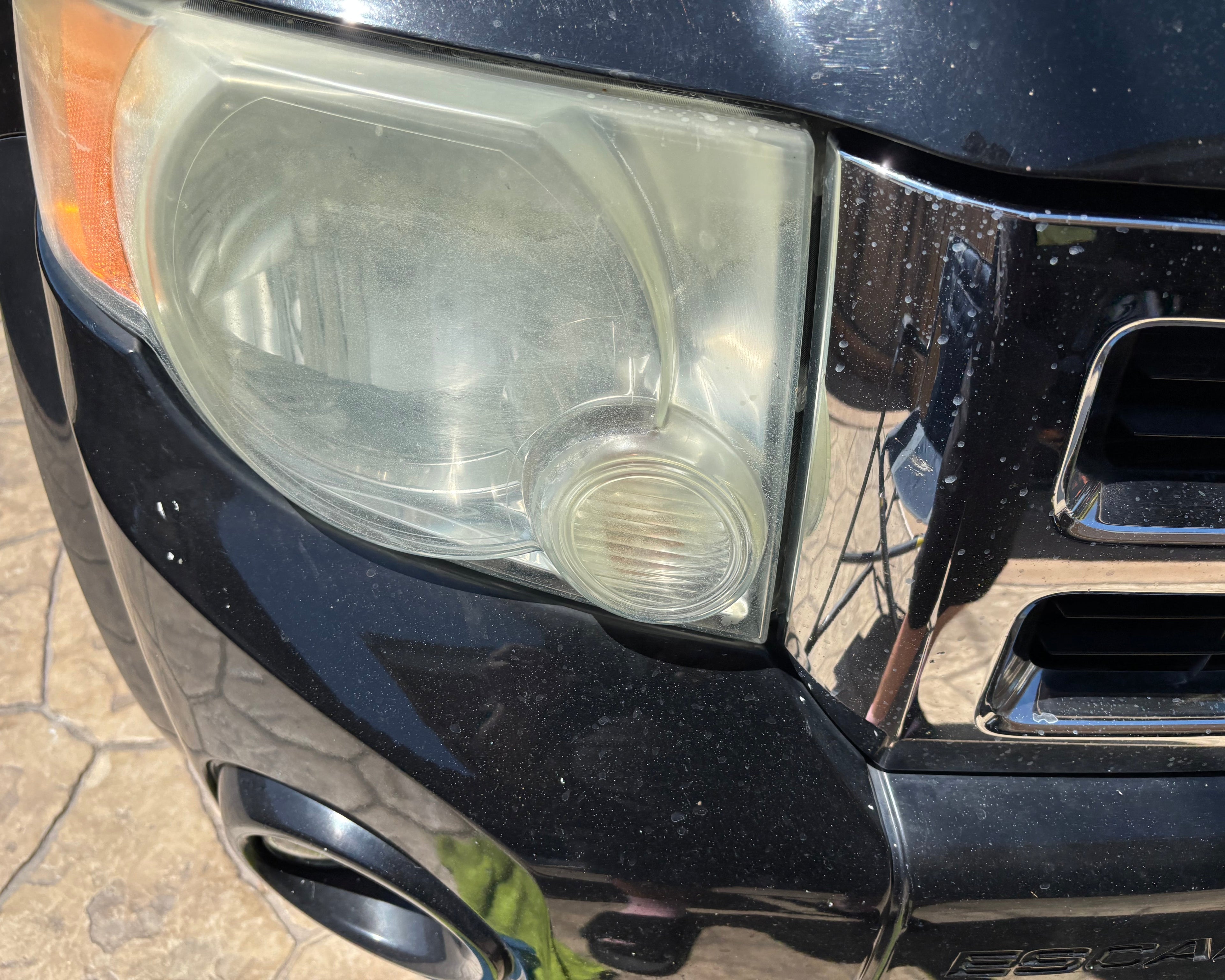 Close-up of a car's front headlight and grille on a pavement background